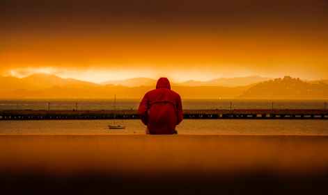 person wearing red hoodie sitting in front of body of water